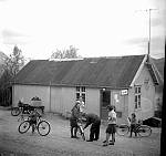 CW1768.jpg    Utenfor butikken i Våtvika.         Christian Waatvik hjelper til å pumpe luft i sykkelhjulet til ei jente fra Barvik, til høyre  Erna Myhre, tror de andre også er fra Barvik.<br>